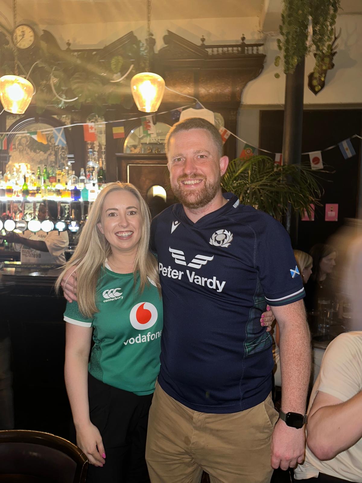 Zara in an Ireland rugby shirt and Alec in a Scotland one, in a pub